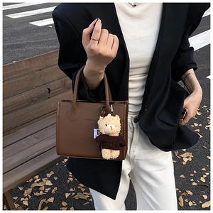 Brown litchi grain leather tote bag with a cute bear charm on an autumn street