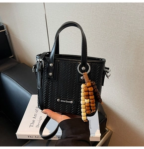 Gros plan du sac à main noir tressé avec plaque métallique et pendentif en perles de bois