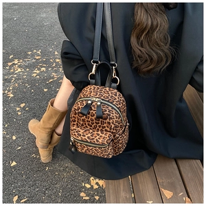 Outdoor lifestyle shot of a leopard print mini backpack with leather straps on a wooden bench
