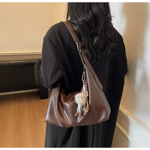 Détail d'un grand sac hobo en cuir marron avec charm peluche porté par un mannequin