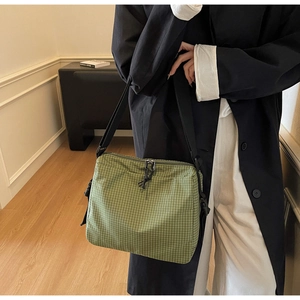 Detail shot of green checkered canvas crossbody bag with adjustable strap on a model