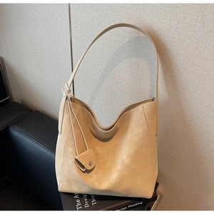 Detail of a beige minimalist hobo bag with a matching mini pendant on a sleek pedestal