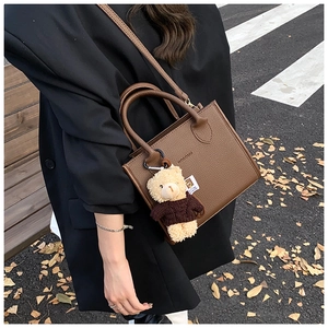 Detail of dark brown lychee leather tote bag with NOGOMU brand logo and bear charm