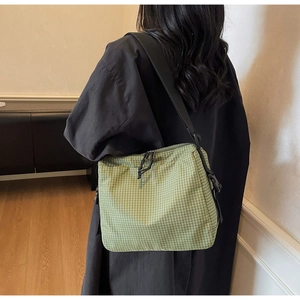 Detail of green checkered canvas bag with zipper closure and adjustable shoulder strap