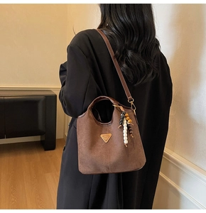Détail d'un sac seau en cuir mat marron avec pompon en perles de bois sur un mannequin