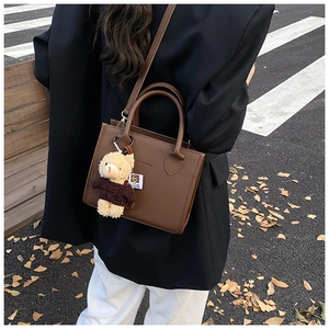 Detail of dark brown pebble leather tote bag featuring a cute teddy bear charm
