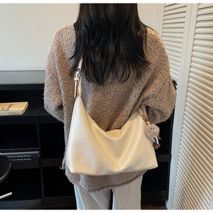 Detail of beige crescent shoulder bag featuring smooth leather and plush charm on the strap