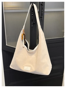 Détail du sac hobo en daim beige avec breloque en perles de bois et logo en cuir gaufré