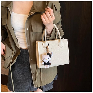 Detail of white lychee leather bucket bag featuring a Hello Kitty plush charm and brand logo