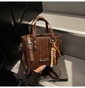 Détail du sac à main marron foncé à texture tissée avec logo argenté et pompon en perles