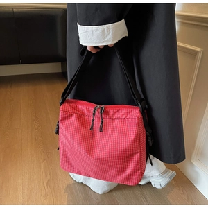Detailed view of red plaid canvas messenger bag featuring adjustable black straps and buckles