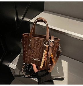 Détail du sac seau marron à texture tressée avec breloque en perles de bois sur livre