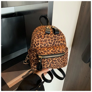 Detailed view of leopard print backpack featuring black leather straps and metal zippers