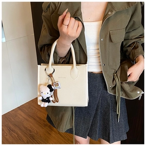 Close-up of cream textured leather tote bag featuring a brand logo and cute plush charm
