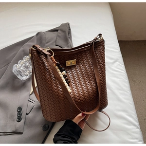 Detail der dunkelbraunen geflochtenen Beuteltasche mit Goldschnalle und Perlenanhänger
