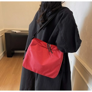 Detail of red plaid canvas bag with adjustable black strap worn over a stylish black coat