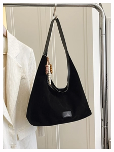 Détail du sac hobo en cuir mat noir avec pompon en perles de bois et écusson en cuir