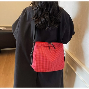 Detail of red checkered canvas crossbody bag with black zipper and adjustable strap