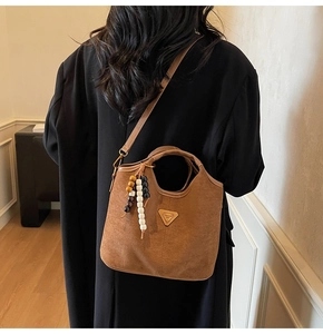 Détail d'un sac seau marron mat avec breloque perlée colorée et emblème métallique