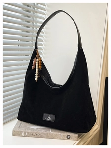 Détail du sac hobo noir montrant la texture suède mate et le gland de perles de côté