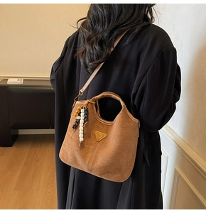 Détail du sac seau en daim marron mat avec pompon en perles et plaque logo en métal