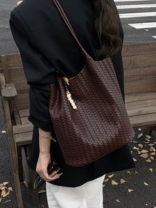 Brown woven leather tote bag with beaded pendant shown in a stylish outdoor setting