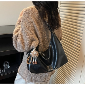 Détail du sac à bandoulière noir en simili cuir avec breloque boule de poils marron