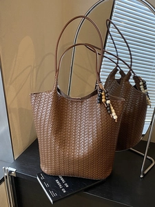 Deep brown woven tote bag with wooden bead charm in a soft light indoor setting