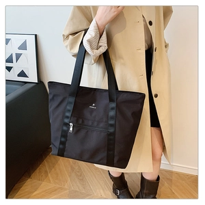 Gros plan du grand cabas noir en tissu oxford avec logo M blanc et poche zippée devant