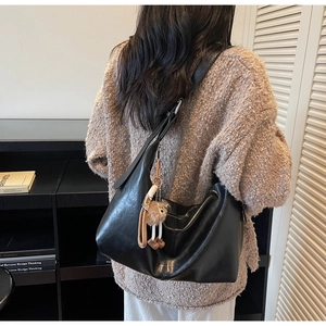 Close-up of black retro leather hobo bag with a cute brown plush bear pendant charm
