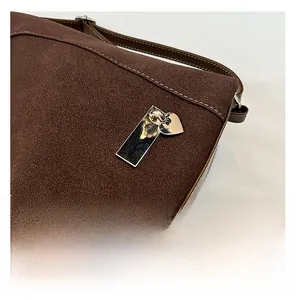Close-up of brown suede shoulder bag featuring white stitching and gold metal charms