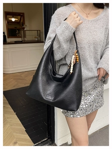 Détail du sac hobo noir avec pompon en perles de bois dans un café au décor minimaliste