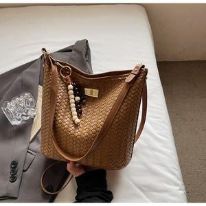 Detailansicht der braunen geflochtenen Eimertasche mit Perlenquaste und goldenem Drehverschluss