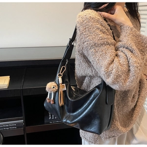 Vue détaillée du sac croissant en cuir noir avec pompon en peluche et franges