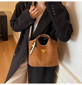 Détail du sac seau marron mat avec logo triangle doré et breloque ethnique perlée