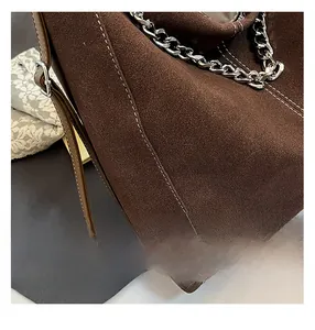 Detail of dark brown suede tote with white stitching and silver metal chain strap