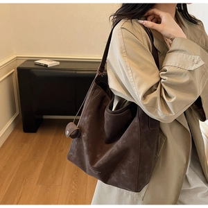 Detail of dark brown suede tote bag featuring a decorative knot and brand logo
