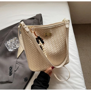 Detail der beige geflochtenen Beuteltasche mit goldenem Metalldrehverschluss und Perlenanhänger