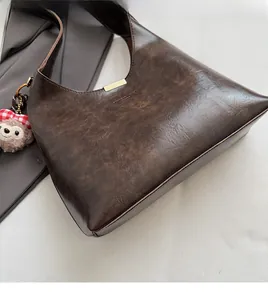 Detail of caramel brown faux leather underarm bag with gold accents and plush bear charm