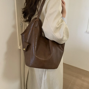 Detail view of large dark brown tote bag with smooth leather texture and side pocket
