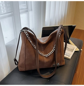 Close-up of brown vintage suede tote bag with thick silver chain and white stitching