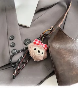 Detail of plush cartoon charm with plaid bow attached to a brown leather shoulder bag