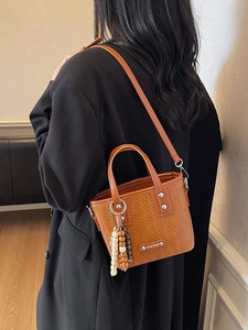 Sac seau tressé marron avec charme en perles de bois porté sur un manteau en laine noir