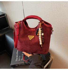 Détail du sac seau bordeaux en cuir givré avec pompon en perles et plaque logo dorée