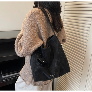 Detail of a large matte black tote bag with elegant brand lettering and side charm accessory