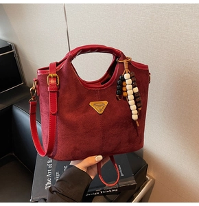 Détail du sac seau rouge mat avec breloque en perles et plaque logo triangulaire