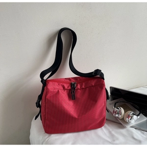 Close-up of red plaid canvas tote bag with adjustable black strap and dual zipper closure