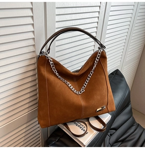 Detail of caramel suede tote bag with silver metal chain and leather handle on a cushion
