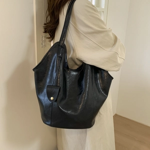 Detail of black glossy leather tote bag with gold buckle pocket on a model's shoulder
