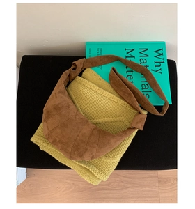 Détail du sac croissant en daim marron avec bandoulière nouée sur un tricot jaune